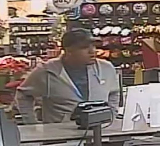 Store footage photo of male burglary suspect wearing a dark colored baseball cap, gray hoodie and dark colored crew neck shirt.